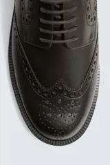 Zapato de vestir acordonado de cuero color marrón oscuro, con puntera brogue y suela de goma.