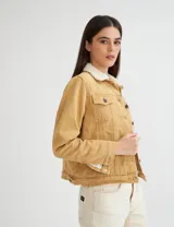 Campera de gabardina color mostaza, forrada con corderito color crudo en el cuerpo y cuello. Tiene corte clásico y botones metálicos personalizados.