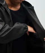 Chaqueta masculina de poliuretano color negro, con diseño de capucha, cierre frontal completo y puños elásticos. Presenta un acabado liso y estructura robusta.