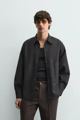 Sobrecamisa de corte relajado confeccionada en denim de algodón con diseño a rayas verticales. Presenta cuello solapa, cierre frontal de botones, manga larga con puños abotonados y un bolsillo plastrón en el pecho.