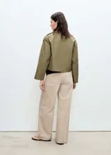 Chaqueta corta de estilo trench con cuello de solapa y cierre frontal de doble botonadura. Presenta diseño recto, manga larga y bolsillos laterales, confeccionada en tejido de mezcla de algodón con forro interior.