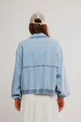 Campera bomber oversize de denim suave, color azul claro con efecto gastado, cierre frontal metálico y elástico en puños y cintura.