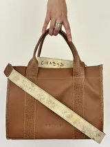 Cartera marrón de cuero genuino con doble asa corta y correa bandolera estampada con la frase "Chabas, soy real, no perfecta".