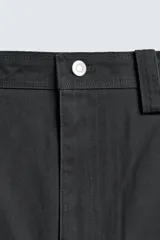 Pantalón de corte relajado confeccionado en tejido de algodón. Presenta cintura con trabillas laterales ajustables, bolsillos frontales y traseros, y un diseño distintivo de costuras laterales giradas que recorren la pernera.