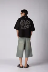 Camisa de manga corta negra 100% algodón, con calce boxy, cuello camisero, cierre frontal con botones y detalle de bordado blanco en la parte inferior.