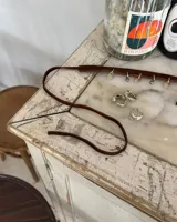 Gargantilla tipo choker de gamuza con dijes colgantes artesanales de metal y perlas naturales. Cuenta con tiras largas para atar y ajustar en la parte posterior.