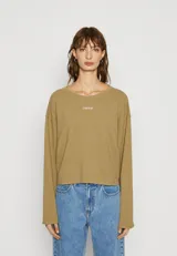 Buzo de cuello redondo en color verde oliva, confeccionado en tejido de algodón con textura. Presenta un corte holgado, mangas largas con hombros caídos y un pequeño logo bordado en el centro del pecho.