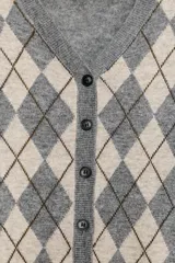 Chaqueta de punto color gris, con cuello pico y manga larga. Presenta un diseño de rombos (argyle) en tonos beige y negro en el frente. Cierre frontal con botones oscuros.