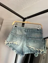 Short de jean celeste con lavado ácido, tiro alto, corte ajustado, bolsillos traseros con bordados y terminaciones desflecadas.