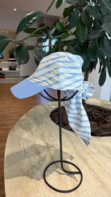 Gorro tipo visera con pañuelo integrado de algodón a rayas celestes y blancas, con detalles de bordado manual en hilo amarillo.