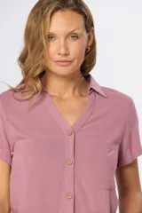 Camisa lisa de lino color beige, de manga corta, con cuello camisero, bolsillo ojal en el pecho y cierre frontal con botones.
