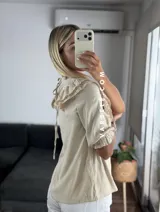 Blusa de símil lino color beige, con cuello redondo fruncido, doble volado en los hombros con detalle de encaje y manga 3/4.