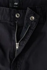Pantalón de corte relajado confeccionado en tejido ripstop resistente. Presenta cierre con botón, bolsillos laterales al bies y bolsillos traseros de parche. Incluye costuras horizontales en las piernas y cordón ajustable en los bajos.