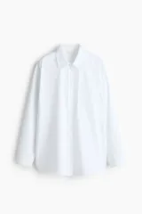 Camisa blanca oversized de manga larga, con cuello clásico, cierre frontal de botones, un bolsillo aplicado en el pecho y dobladillo redondeado.