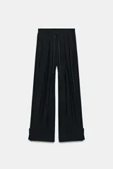 Pantalón fluido de tiro medio confeccionado en mezcla de modal, con cintura elástica ajustable mediante cordones. Presenta pinzas en el delantero, bolsillos laterales ocultos y bajo ajustable con trabilla y botón a presión.