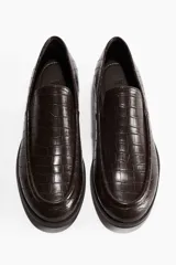 Mocasines de hombre en tejido revestido con textura efecto piel de cocodrilo en color marrón oscuro, con costura frontal tradicional y suela plana con pequeño tacón.