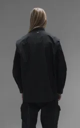 Chaqueta tipo overshirt de microfibra, color negro, con calce oversize y ruedo curvo. Presenta cierre frontal con broches a presión, bolsillos frontales de gran tamaño y cierres laterales a lo largo de las mangas para ajustar su amplitud.