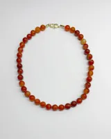 Collar corto compuesto por cuentas esféricas de piedra ágata en tonos naranjas y rojizos, con cierre metálico dorado.