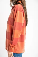 Sweater tipo polo de algodón peinado con diseño de rayas horizontales en tonos rojizos y terracota, cuello camisero y mangas largas con puños.