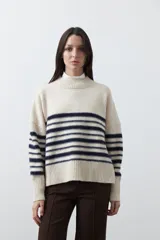 Polera de tejido de punto con diseño a rayas horizontales en color azul marino sobre base beige. Presenta cuello alto, mangas largas con puños acanalados y una silueta relajada.