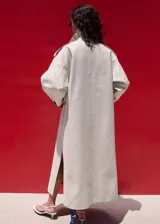Chaqueta larga de algodón color beige, de diseño recto con cuello en pico y solapas con muesca. Cuenta con cierre delantero de doble botonadura, bolsillos laterales y mangas largas reversibles.
