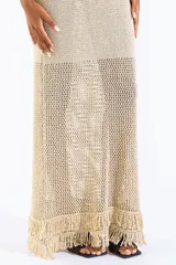 Vestido largo de punto abierto con sutil brillo dorado, escote en V y diseño sin mangas con detalles de flecos en el ruedo.
