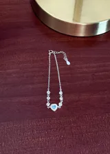 Pulsera de plata 925 con cadena de eslabones finos, decorada con pequeñas zirconias blancas engarzadas y un dije central en forma de corazón con una zirconia celeste rodeada de zirconias blancas.