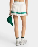 Minifalda de tenis blanca con tableado y cintura elástica. Presenta dos líneas horizontales verdes en el ruedo y logo de la marca en la cintura.
