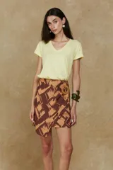 Minifalda marrón con estampado abstracto en tonos beige, corte tipo wrap y hebilla redonda de madera en la cintura.