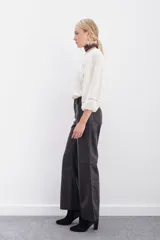 Pantalón de cuero ovino con corte oxford y tiro medio. Presenta diseño de cinco bolsillos, cierre frontal con botón metálico y costuras horizontales a la altura de la rodilla.
