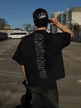Remera negra oversize de manga corta, con estampa tipográfica vertical en la espalda y logo pequeño en el frente.