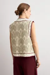 Chaleco capitoneado sin mangas, de color blanco con estampado paisley en tonos beige y verde, con ribetes en color bordó.