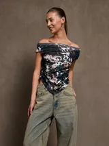 Top negro de manga corta con escote Bardot (hombros descubiertos) y detalle de drapeado o fruncido que termina en punta en el centro inferior.