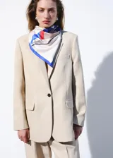 Blazer Paola de corte recto, color beige, confeccionado en mezcla de lana y lino. Presenta cuello pico con solapa, mangas largas, un bolsillo de ribete en el pecho, dos bolsillos con solapa en los laterales y cierre frontal de un botón oscuro.