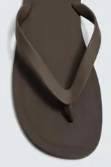 Sandalia tipo ojota o chancleta de goma, con base de color verde oscuro y tiras negras. Presenta una suela plana.