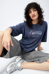 Remera azul de manga corta con estampa de caballo y texto "It's about to get WESTERN".