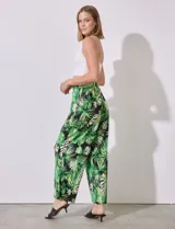 Pantalón largo de seda fría estampada con hojas de palmera en tonos verdes y blancos sobre fondo negro. Tiene pretina ancha elastizada.