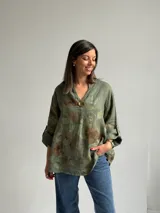 Blusa verde de lino con estampado de flores grandes en tonos marrones y verde oliva, con cuello en V y un botón decorativo central.