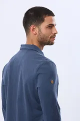 Remera polo de manga larga confeccionada en tejido jersey, con cuello clásico y cierre frontal de tres botones. Presenta un diseño liso con un pequeño logo bordado en el pecho y una etiqueta decorativa en el ruedo.