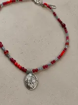 Gargantilla de cuentas de cristal en tonos tornasolados, violetas y oscuros, con dije central ovalado de metal plateado con diseño de escudo.