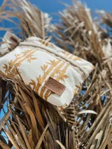 Sobre de tela color crudo con estampado de cañas color mostaza, detalles en yute y pulsera personalizada.