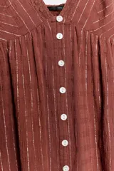 Vestido mini marrón terracota con finas rayas verticales de hilo metalizado, escote en V, tirantes finos ajustables, cierre frontal con botones y detalle de volados desflecados en el borde inferior.