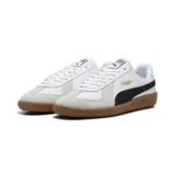 Championes Puma modelo Army Trainer, color blanco con detalles en negro y superposiciones de gamuza gris claro en la puntera. Cuenta con suela de goma tipo 'gum' y la inscripción de la marca en dorado en el lateral.