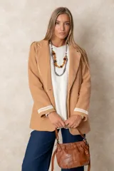 Blazer de lana soft color beige, con cierre frontal de un botón, solapas clásicas y dos bolsillos frontales con detalles de bordado artesanal en relieve. Presenta un diseño estructurado y elegante.