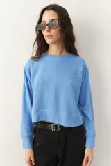 Buzo corto de manga larga con cuello redondo, confeccionado en tela texturizada. Presenta un diseño holgado con costuras decorativas en el frente y puños acanalados.