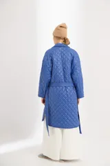 Campera azul capitoneada de nylon con forro de algodón y relleno de poliéster. Tiene ruedo curvo, largo midi, cinta para atar a la cintura y bolsillos delanteros.