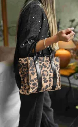 Cartera mini tipo tote bag con estampado animal print, doble asa corta de cuero sintético negro y cierre superior.