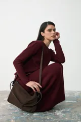 Cartera de hombro confeccionada en gamuza color chocolate, con cierre superior y doble sistema de correas: una fija de cuero liso negro para llevar al hombro y una correa larga ajustable y extraíble de gamuza y cuero negro para usar cruzada.