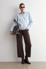 Blusa de algodón color celeste, con cuello camisero, escote en V y mangas largas con puños anchos. Presenta un diseño de corte recto y holgado.
