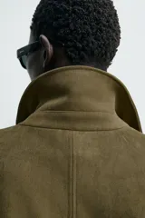 Cazadora cropped fit color verde militar, confeccionada en tejido efecto ante. Cuenta con cuello solapa, manga larga con puño abotonado, trabillas en los hombros, bolsillos laterales ocultos y un bolsillo interior. El bajo tiene elástico interior y el cierre frontal es con cremallera oculta por solapa con botones a presión.